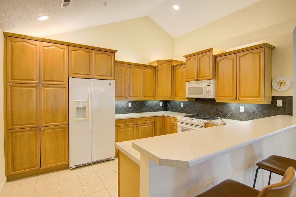 Wood kitchen cabinets, white appliances and kitchen backsplash at 7101 Meadowsweet Lane, Shawnee, KS 66227