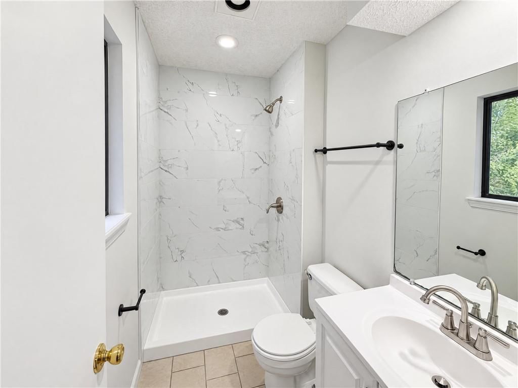 Tiled shower, frameless glass shower and white vanity at 14416 Saint Andrews Drive, Grandview, MO 64030